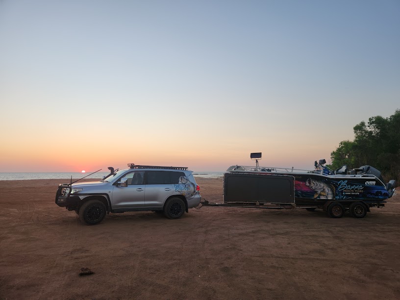 SUV towing a boat on a trailer at sunset by the beach.