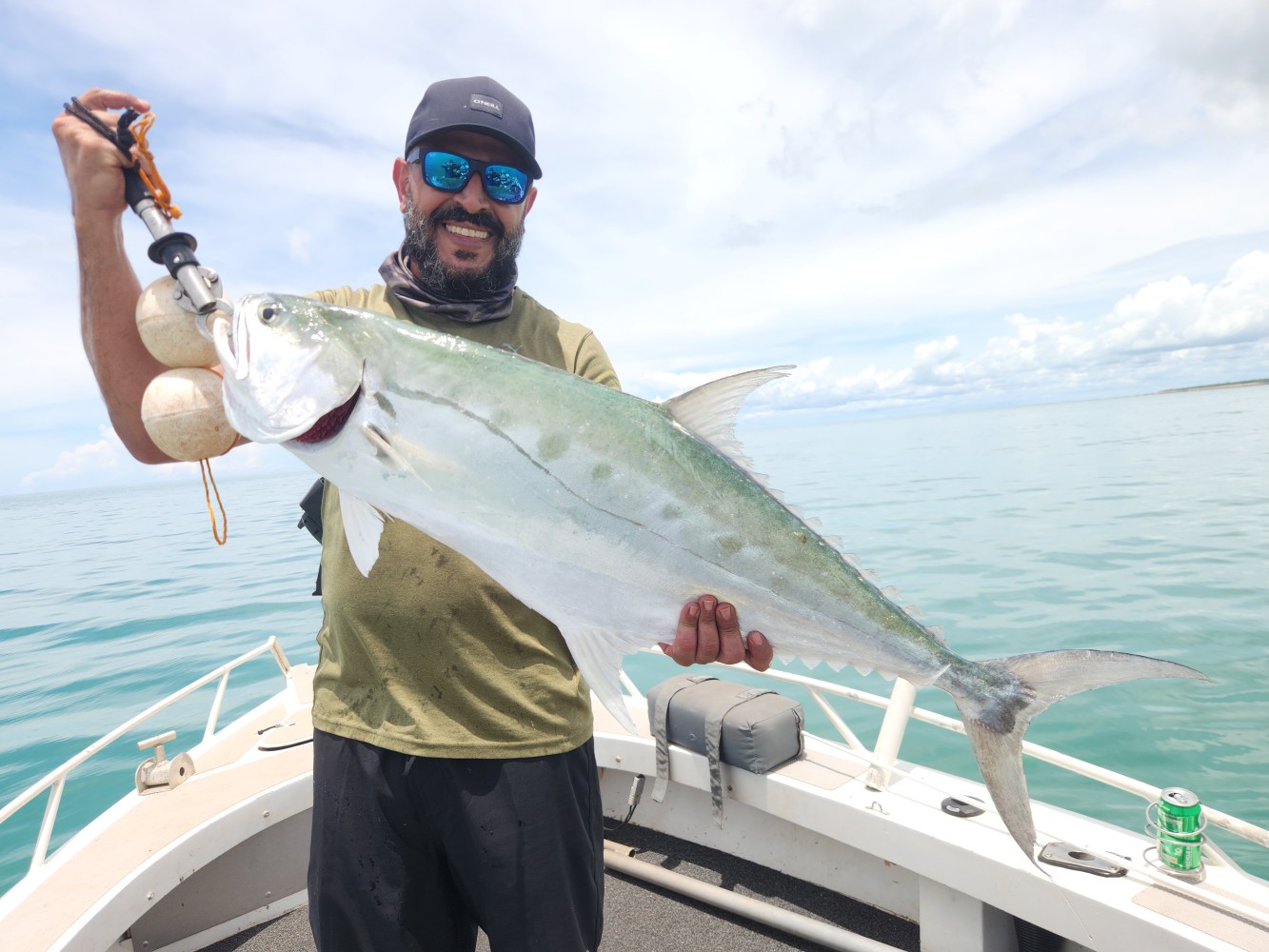 Man on a boat holding a large fish with the ocean and sky in the background.
