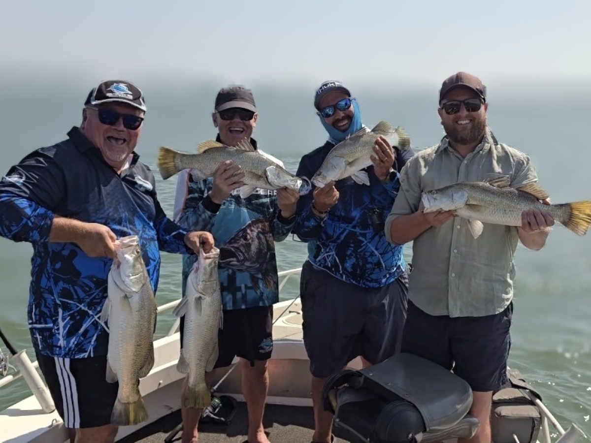 Four men on a boat holding large fish, smiling with ocean in the background.