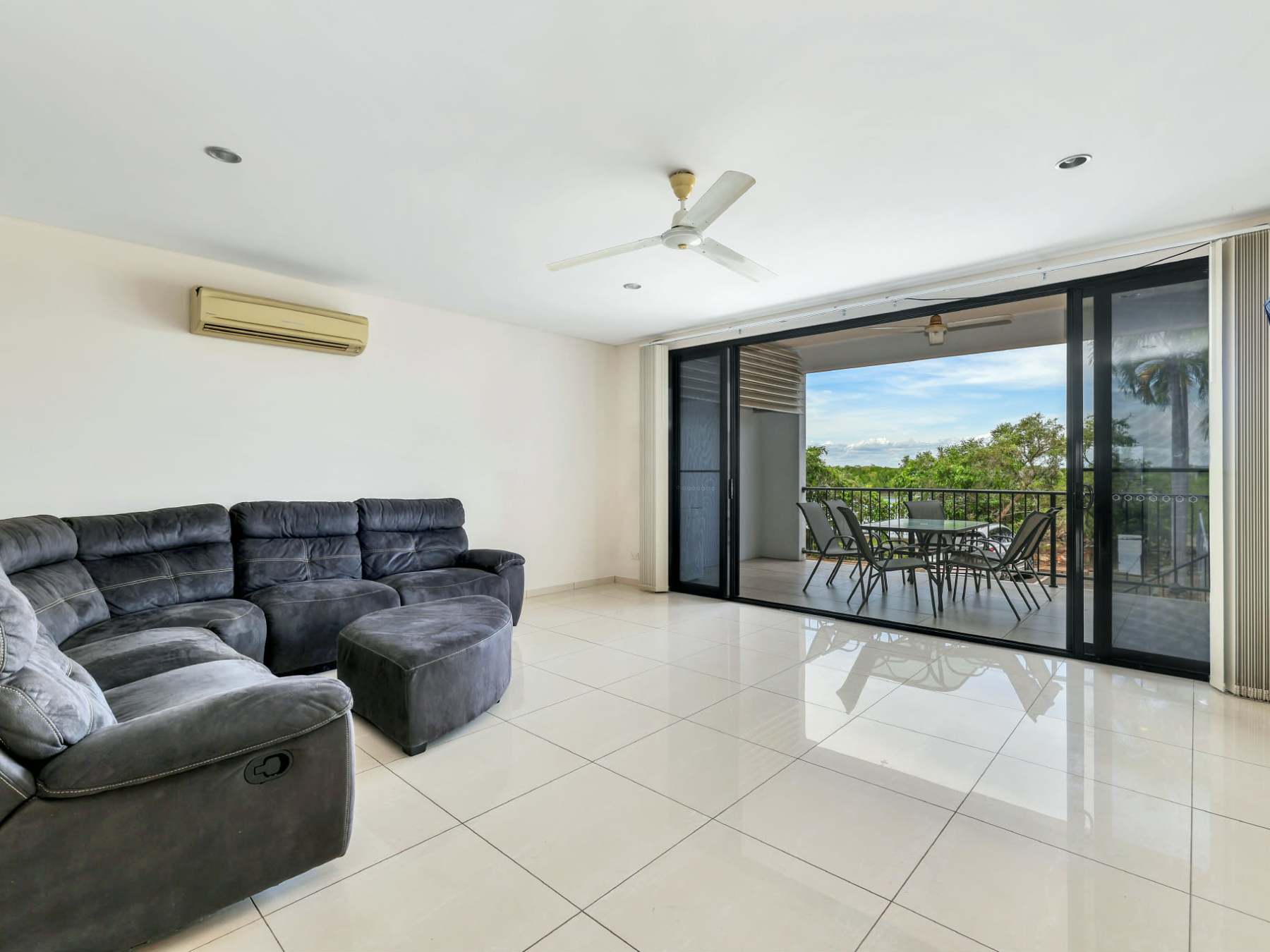 Modern living room with black sofa, TV, balcony view, and sliding glass doors.