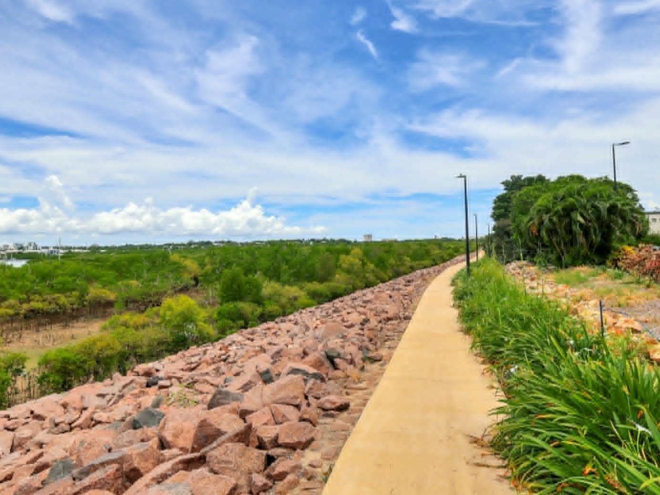 Pathway with rocks and greenery under a blue sky with clouds.