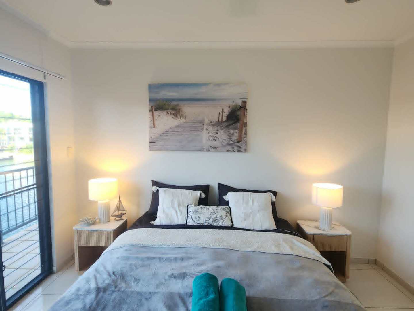 Cozy bedroom with a double bed, pillows, blankets, and two folded towels; bedside lamps illuminate the room.