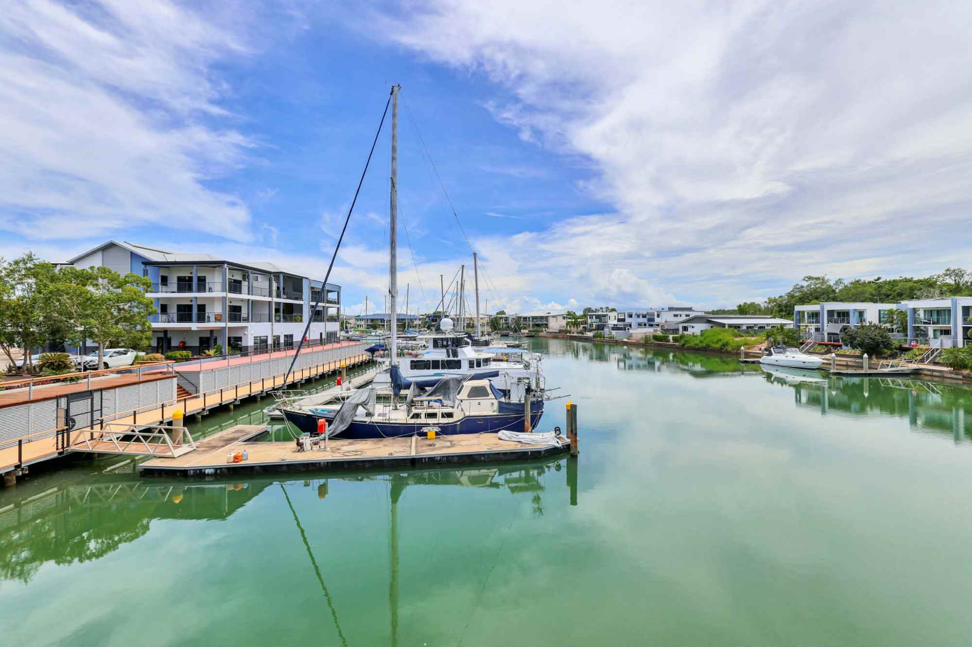 Boats docked on calm water near modern buildings under a cloudy sky.