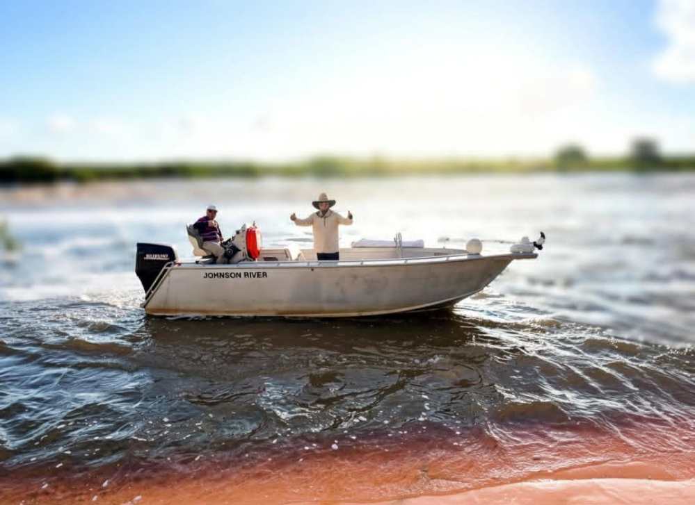 Two people on a small motorboat named 'Johnson Rover' on a sunny day.