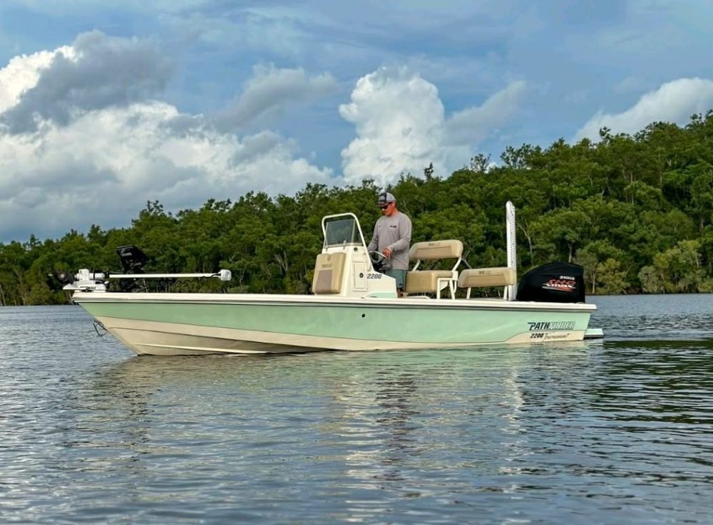 Person standing on a motorboat in a calm river with cloudy sky.