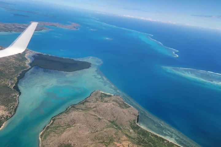 Aerial view of ocean, islands, and airplane wing over clear blue water.