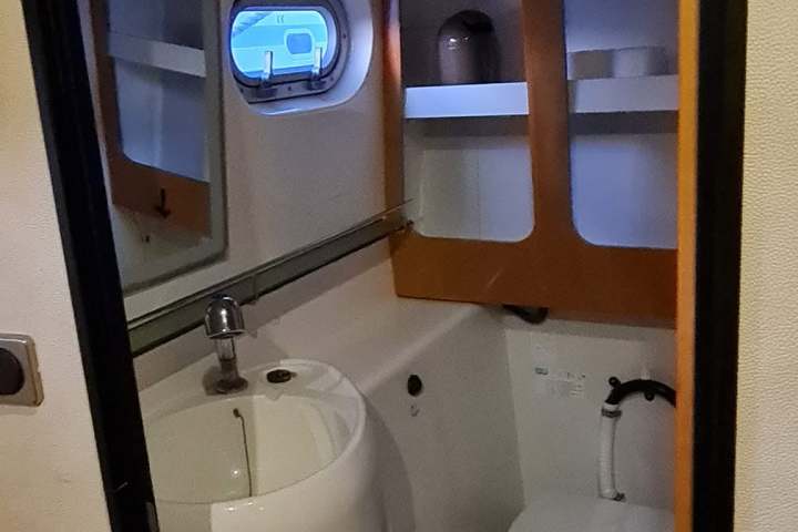 Compact boat bathroom with toilet, sink, and mirror, small window above.