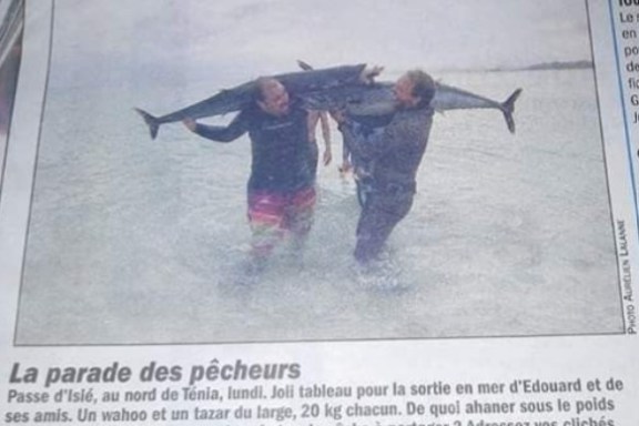 Two men carrying a large fish through shallow water.