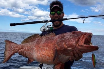 Person holding large fish with fishing rod on a boat.