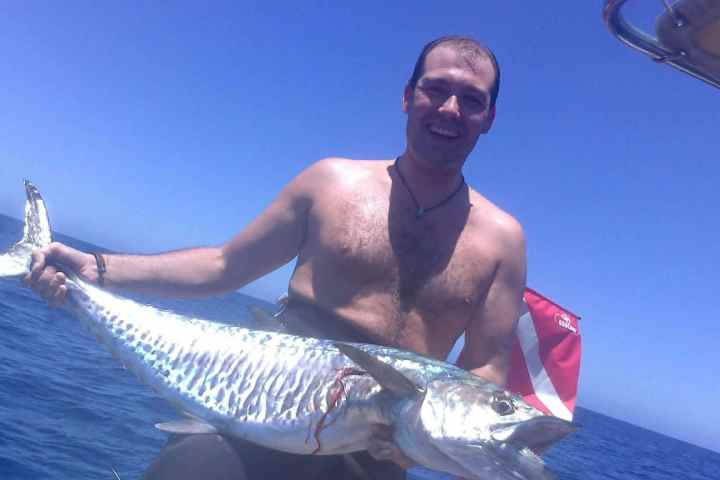 Man holding a large fish on a boat under clear blue sky.