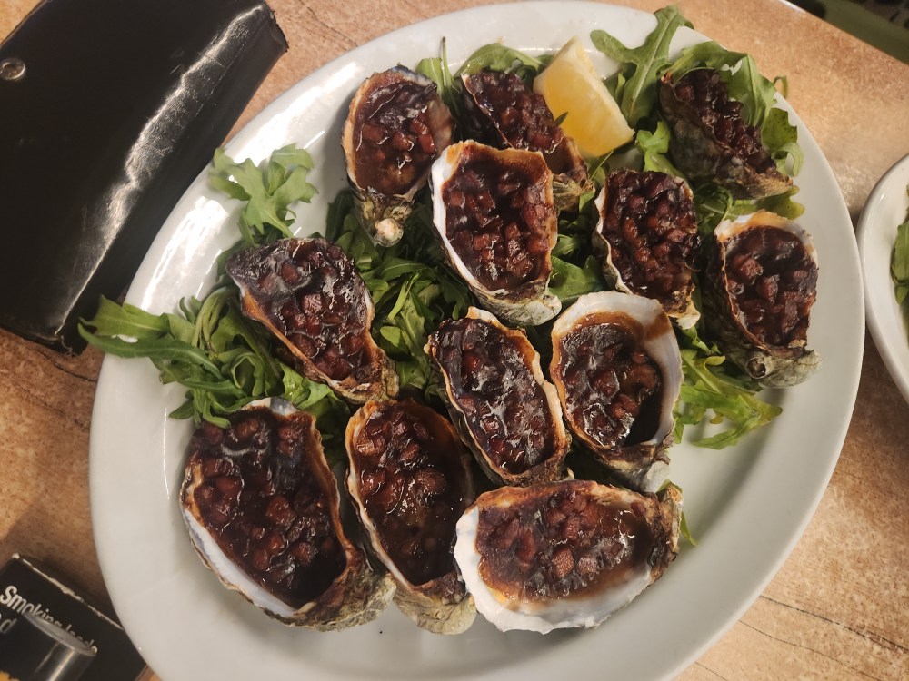 Grilled oysters on a bed of greens with a lemon wedge on a plate.